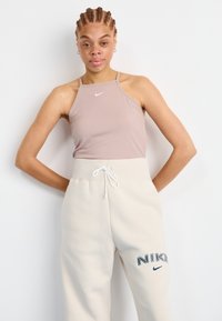 Světle růžový top na krk s bílým logem; krémové tepláky s vyšitým námořnickým logem "NIKE"; materiál směs bavlny, volný střih.
