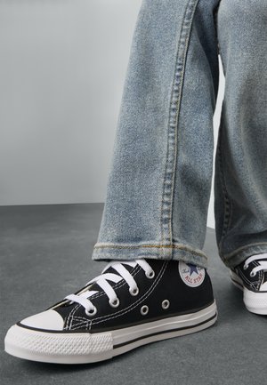 Baskets noires en toile avec semelles en caoutchouc blanc et embout blanc, dotées de lacets et d'œillets blancs. Jean en denim bleu avec un aspect délavé.