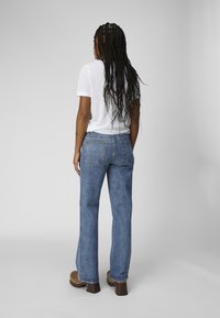 Lett hvit t-skjorte kombinert med høytlivede blå denimjeans. Jeansene har baklommer og rett ben. Brune hælklomper.