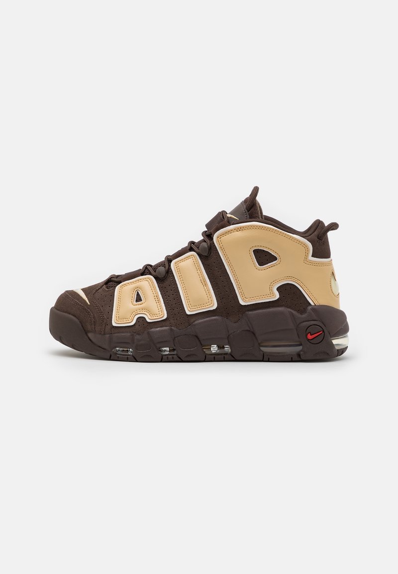 Brown sneaker with beige accents, featuring large "AIR" lettering. High-top design, textured surface, visible cushioning, and red logo detail.