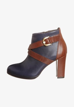 Botín de tacón alto en marrón y marino con un acabado de cuero liso, que presenta una correa diagonal y un detalle de hebilla dorada.