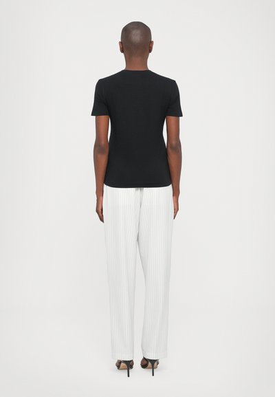 T-shirt noir ajusté à manches courtes, associé à un pantalon large à rayures blanches et des sandales à talons, vu de l'arrière.
