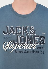 Ανοιχτό μπλε βαμβακερό μπλουζάκι, με έντονη επιγραφή: "JACK & JONES SUPERIOR wrd. New Aesthetics" σε σκούρα και λευκή γραμματοσειρά.