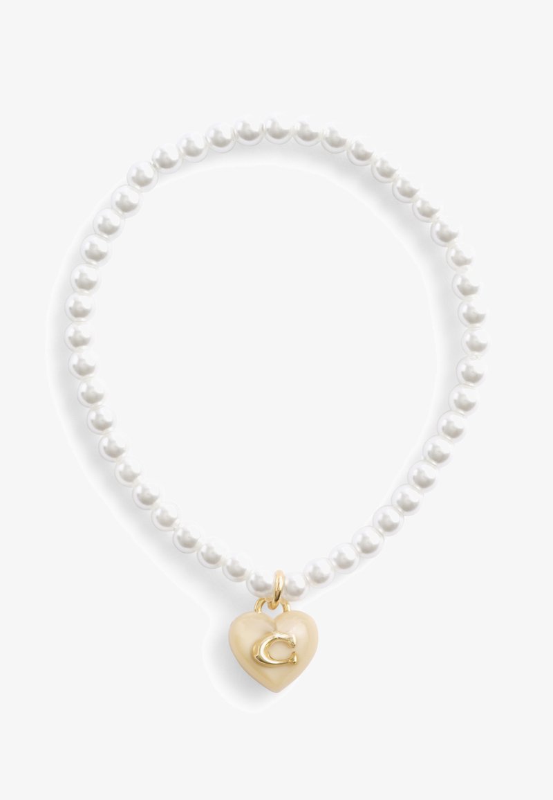 Pulsera de perlas con un charm en forma de corazón en tono dorado. El charm es de color beige claro y tiene una letra "C" grabada. Las perlas blancas, espaciadas uniformemente, forman la pulsera.