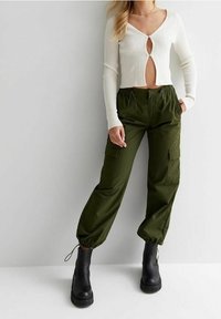 Bílý žebrovaný cropped svetr s dírou v dekoltu, kombinovaný s olivově zelenými cargo kalhotami s kapsami a elastickými manžetami. Černé platformové boty.