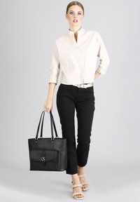 Borsa tote nera con una tasca frontale piatta decorata con borchie dorate, doppio manico superiore e un design strutturato. Texture in pelle liscia.