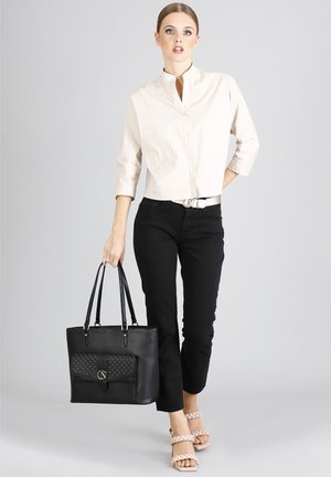 Bolso tote negro con un bolsillo frontal plano adornado con tachuelas doradas, doble asa superior y un diseño estructurado. Textura de piel suave.