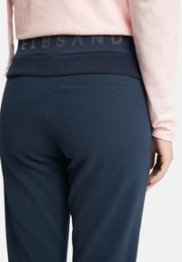 Marineblaue Sweatpants mit einem breiten elastischen Bund und einem Logo; glatte Textur und schmale Passform, hervorgehoben durch eine dezente Gesäßtasche.