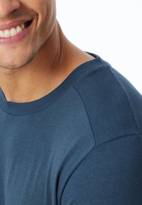 Dunkelblaues Kurzarm-T-Shirt mit einer glatten Textur und geripptem Ausschnitt. Die Schulter hat einen dezenten strukturierten Akzent.