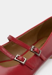 Ballerines en cuir rouge avec deux sangles ajustables munies de boucles en métal argenté. Texture lisse et design à bout arrondi.