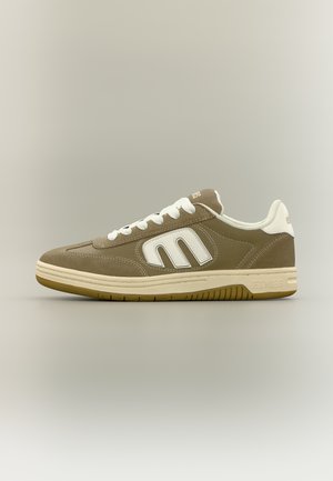 Brauner und beiger Sneaker mit niedrigem Schaft, weißen Schnürsenkeln und großem weißem "M"-Logo an der Seite, beiger Sohle und "Etnies"-Markierung an der Ferse.