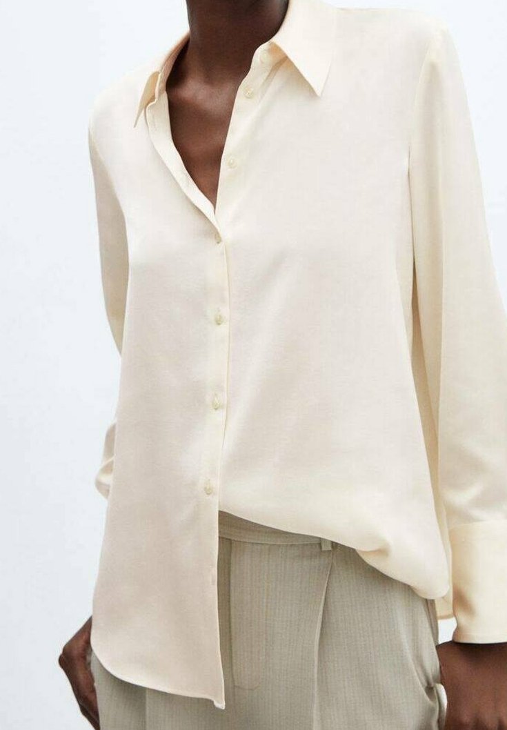 Femme portant une chemise ample crème boutonnée à manches longues et un pantalon beige taille haute.