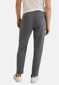 Pantalones gris a rayas con un ajuste entallado, que presentan un frente plano, dos bolsillos traseros con botones y puños doblados, combinados con zapatillas blancas.