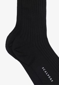 Calcetines negros acanalados hechos de un material suave, con refuerzo en el talón y en la puntera. El nombre de la marca "SCALPERS" está impreso en blanco.