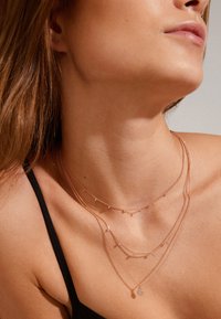 Collares en oro rosa en capas que presentan longitudes variadas, cadenas delicadas, pequeñas cuentas y un colgante central con un diseño circular.