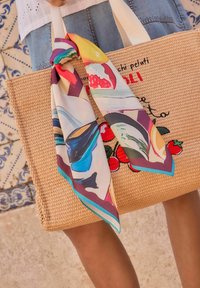 Woven beige tote bag with white handles, featuring colorful printed scarf tied at the top. Design includes embroidered red and green fruit details.