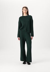 Dark green knitted loungewear set featuring cable patterns. The oversized sweater has a round neckline, and wide-leg pants complement the look.