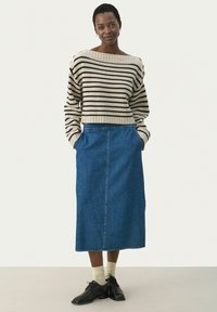 Pull en tricot rayé beige et noir, associé à une jupe midi en denim bleu. La tenue comprend des chaussures noires et des chaussettes claires.