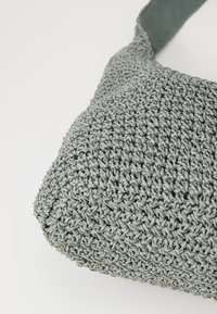 Sac en tissu tissé gris avec une surface texturée, doté d'une bandoulière douce et d'une forme arrondie, idéal pour un usage décontracté.