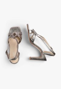 Metallic sølv højhælede sandaler med firkantet tå, krydsede stropper og ankelspænde. Glat tekstur med et strømlinet design.