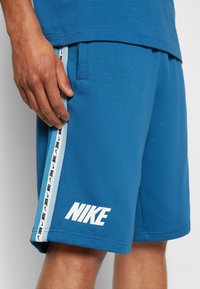 Pantalones cortos azules de Nike hechos de tela suave, con logo blanco, bolsillos laterales y una franja contrastante con marca negra a lo largo de los costados.