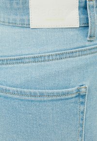 Vaaleansiniset farkut, joissa on ommeltu etutasku, tagi, jossa lukee "Bershka Denim Collection", sekä näkyvä teksturoitu kudontakuosi.