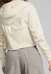 Gemiddeld cropped crèmekleurige hoodie met een trekkoord in de capuchon, geribbelde tailleband en een zachte, gestructureerde stof, gecombineerd met lichtgrijze hoge taillebroeken.