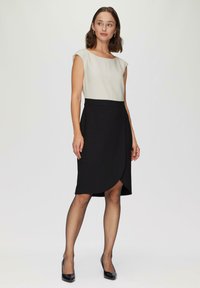 Jupe noire à enrouler avec un haut ajusté gris clair. Manches courtes et tissu texturé. Design jusqu'aux genoux, associé à des talons noirs.