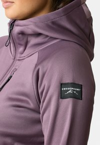 Paarse capuchonjack met een gladde textuur, voorzien van een zwart logo-embleem op de mouw en een trekkoord voor een verstelbare pasvorm.