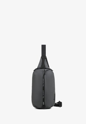 Zwarte sling-rugzak met een voorvak met ritssluiting, verstelbare band en een verticale ritssluiting met merknaam.