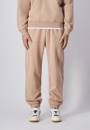 Helle beige Jogginghose mit elastischen Bündchen und lockerer Passform. Getragen mit weißen und schwarzen Turnschuhen, die markante Akzente aufweisen.