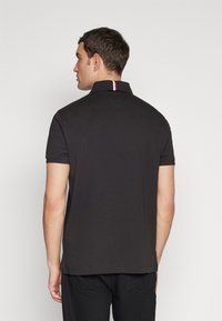 Polo nero con colletto a strisce rosse e bianche a contrasto, maniche corte e vestibilità comoda, realizzato in morbido tessuto di cotone.