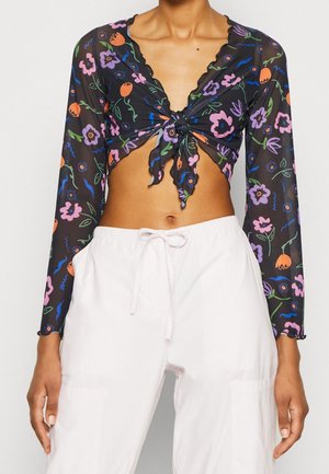 Black sheer long-sleeve crop top with colorful floral print and front tie, worn with white drawstring pants.