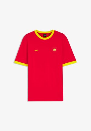 Camisa roja de manga corta con cuello y bordes de las mangas amarillos, texto "BOSS" en el pecho izquierdo y un pequeño emblema de la bandera española en el pecho derecho.