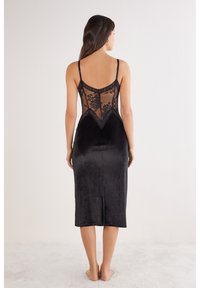 Czarna sukienka z koronkowym tyłem, regulowanymi ramiączkami oraz gładką, satynową częścią sięgającą do kolan. Koronka zawiera kwiatowe wzory i panelowy design.