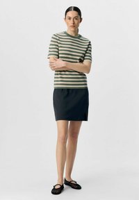 Top a righe lavorato a maglia in beige e verde, abbinato a una gonna nera con uno spacco laterale. Scarpe nere in rete a pianta piatta completano il look.