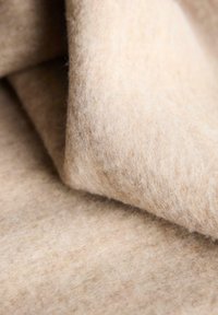 Tessuto di feltro beige con una consistenza soffice e pelosa; strati ripiegati l'uno sull'altro, che mostrano una superficie liscia e sottili variazioni di colore.