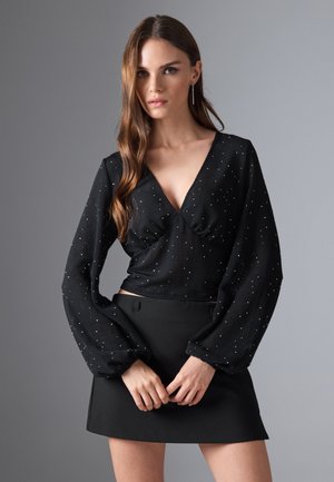 Black long-sleeve top with a V-neck, textured fabric, and silver studs, paired with a form-fitting black mini skirt.