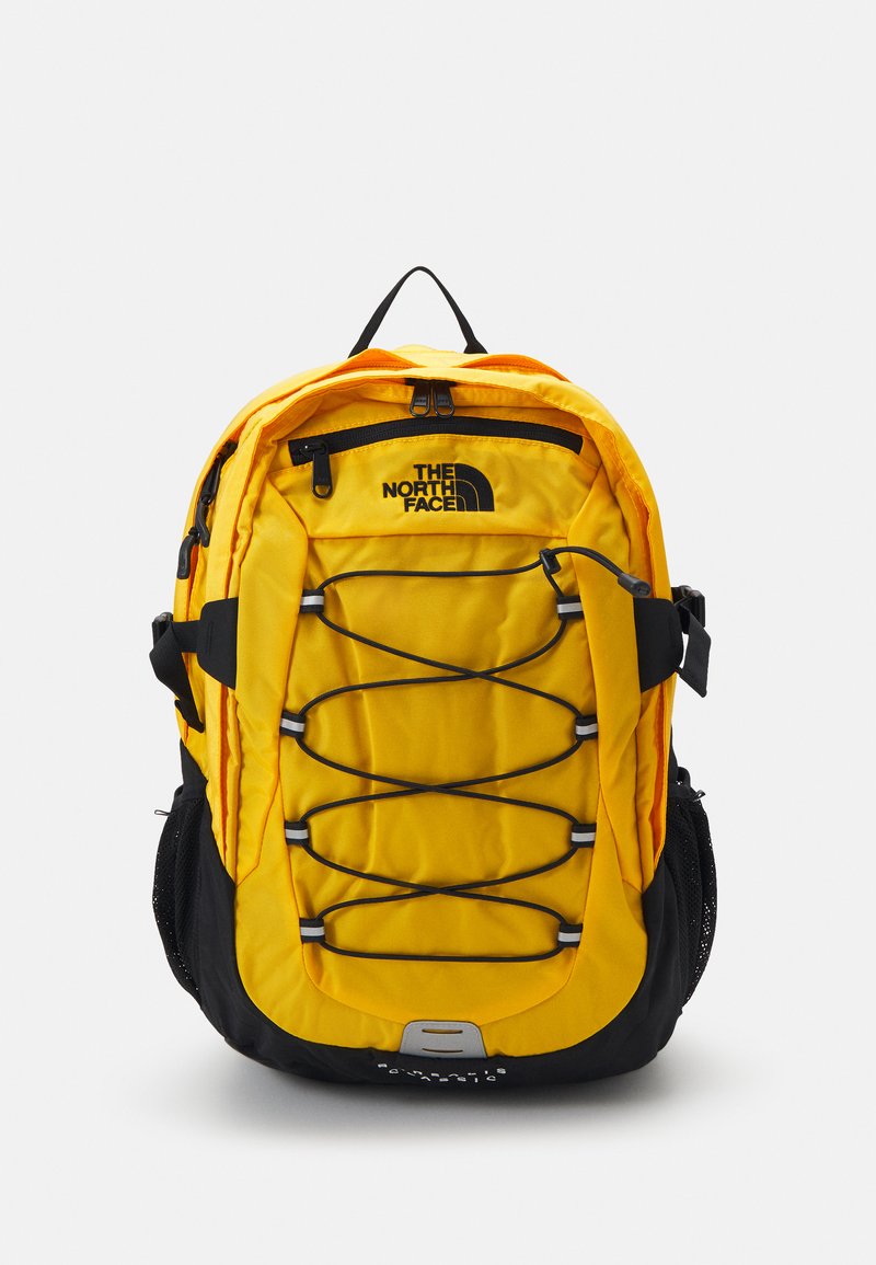 Mochila amarela e preta com acabamento acolchoado, detalhes em corda bungee na frente, bolsos laterais em malha e logótipo na parte superior da frente.