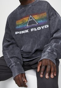 Sudadera gris con un gráfico frontal que presenta un diseño de rayas de arcoíris y un triángulo. El texto dice "PINK FLOYD" en letras blancas en negrita.