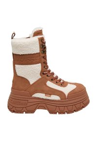 Bota de ante marrón y borrego blanco con cordones, que presenta una suela de goma gruesa con patrones estriados y detalles del logotipo en el costado.