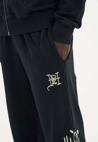 Svarta träningsbyxor i mjukt material, med elastisk midja, sidofickor och detaljer i krämfärgad logotyp.