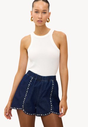 Witte geribde tanktop gecombineerd met donker denim short met een golvende zoom en metalen versieringen langs de zijnaden.
