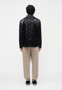 Čierna bundá s geometrickým vzorom, skombinovaná s béžovými nohavicami. Bunda má lesklý, textúrovaný povrch.