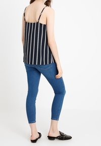 Débardeur bleu marine à rayures verticales blanches, avec fines bretelles et coupe décontractée ; associé à un jean skinny bleu et des chaussures noires à enfiler.