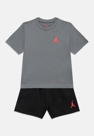 Siva majica s kratkimi rokavi z rožnatim logotipom Jordan na prsih, kombinirana s črnimi kratkimi hlačami z enakim rožnatim logotipom. Iz bombažnega materiala.