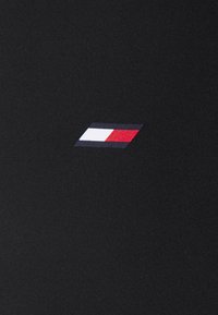 Czarna tkanina o gładkiej fakturze z małym logo. Logo to geometryczny kształt w kolorach czerwonym, białym i niebieskim.