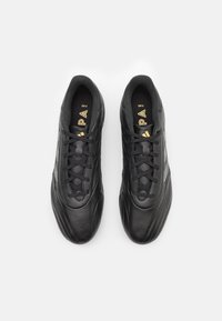 Black athletic shoes with a smooth leather upper, textured detailing, and a structured silhouette. Features black laces and gold logo accents.
