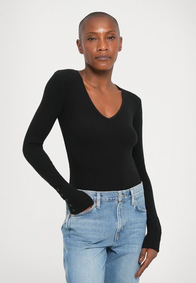 Bodysuit negro de manga larga con escote en V, textura acanalada y detalles de botones en los puños, combinado con vaqueros de tiro alto en azul claro.
