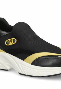 Chaussure noire à enfiler avec une tige texturée, des accents jaunes et une semelle blanche épaisse à crampons en caoutchouc pour une meilleure adhérence.